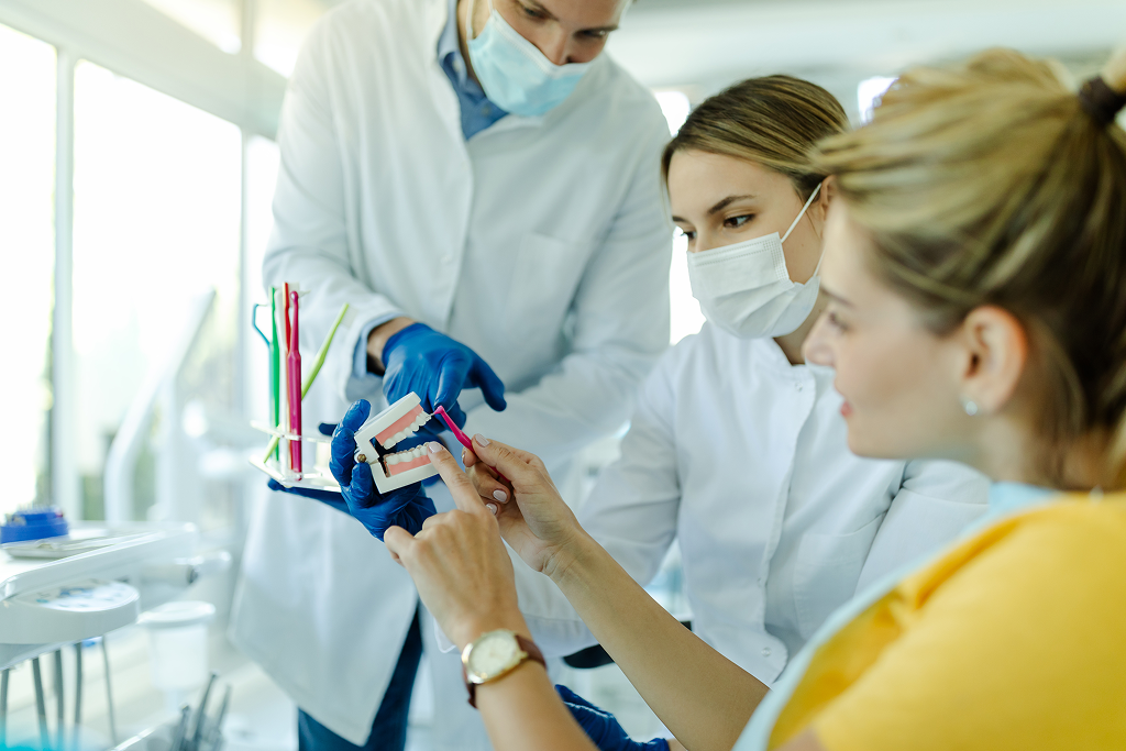 woman cosmetic dentist showing on a jaw model how to clean teeth