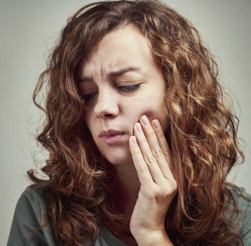 woman in pain holding her cheeks in dental emergency