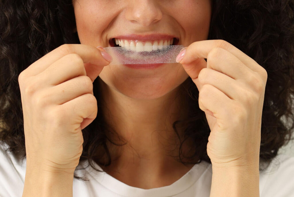 person holding a teeth whitening strip close to their mouth